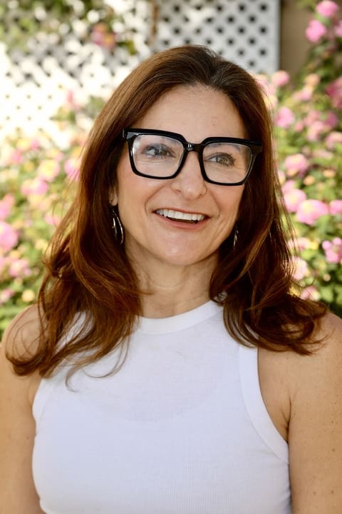 Professional woman with brown hair and glasses looking confidently at the camera, representing leadership coaching, resilience, and organizational change.