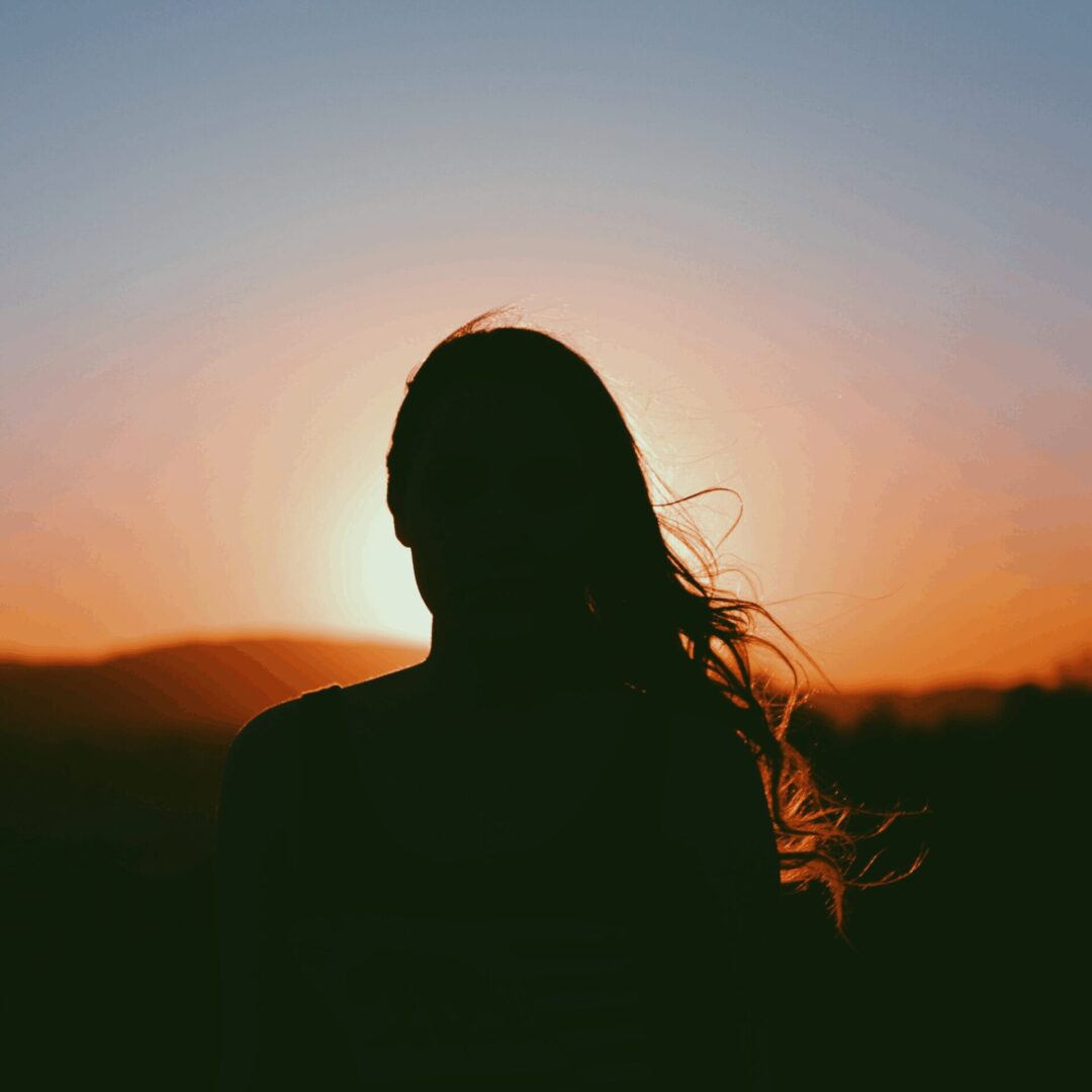 Silhouette of a woman standing outdoors at sunset, representing balance, motherhood, and embracing change.