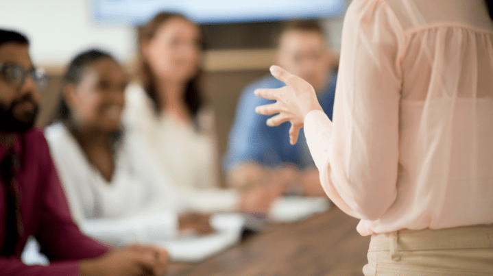A leader speaking to a group of professionals who are actively listening, representing growth in identity, presence, and decision-making during leadership transitions.